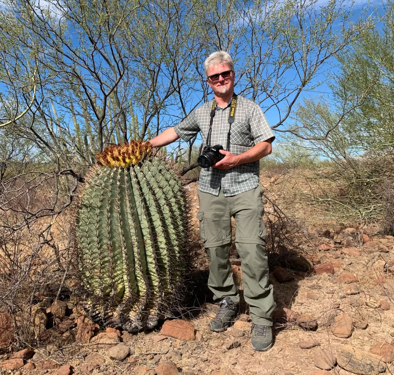 Vereinsmitglied Michael steht neben einem riesigen Ferocactus Exemplar in Mexiko, hinter ihm sind vereinzelne Büsche und Bäume zu sehen